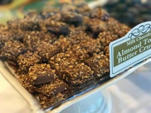 A close-up of milk chocolate almond toffee butter crunch candies, coated in crushed nuts, displayed on a tray.