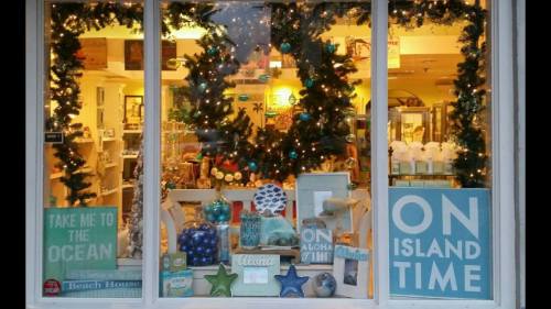 A storefront window decorated with ocean-themed decor, signs, and holiday greenery, promoting a relaxed island vibe.