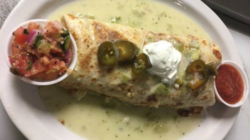 A large burrito topped with jalapeños and sour cream, served with salsa and pico de gallo on the side.