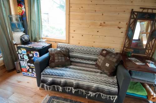 Cozy interior of a cabin featuring a sofa with patterned throw, a water cooler, and wooden walls.