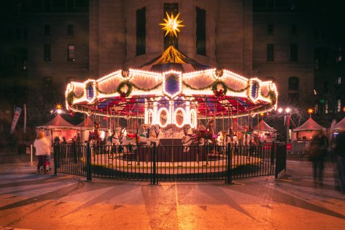 A beautifully lit carousel with festive decorations, surrounded by a bustling holiday market at night.