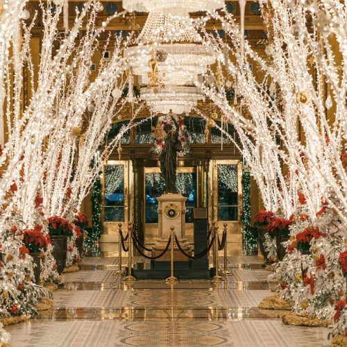 A beautifully decorated hallway with sparkling lights, festive greenery, and a statue, creating a magical holiday atmosphere.