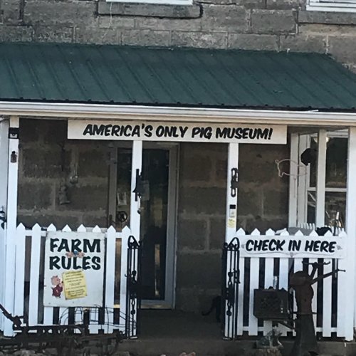 Sign for "America's Only Pig Museum" on a building with a white picket fence and a green roof.