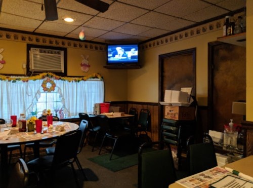 A cozy restaurant interior with tables, chairs, and a TV on the wall, decorated with festive accents.