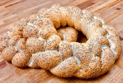 A braided bread loaf topped with sesame seeds, resting on a wooden surface.