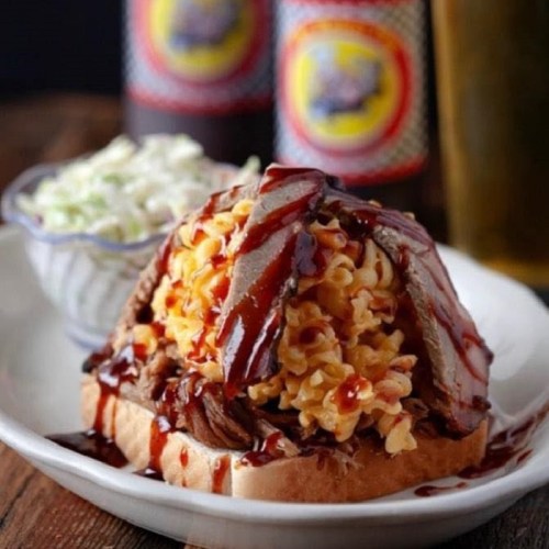 A sandwich topped with pulled pork, macaroni and cheese, and barbecue sauce, served with a side of coleslaw.