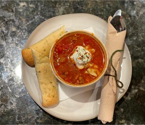 A bowl of hearty soup topped with cream and herbs, served with two pieces of bread on a plate.