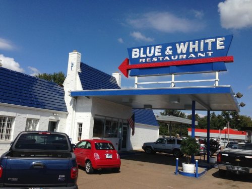 Exterior of Blue & White Restaurant with a blue roof, sign, and parked cars under a clear blue sky.