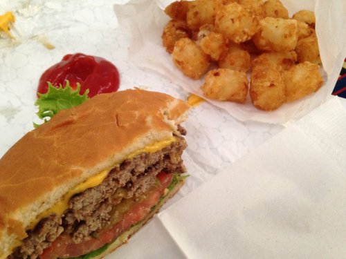A cheeseburger with lettuce, tomato, and pickles next to a serving of crispy tater tots and a side of ketchup.