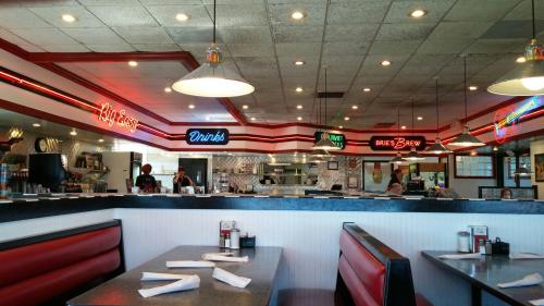 A retro diner interior with red booths, neon signs, and a bustling kitchen in the background.