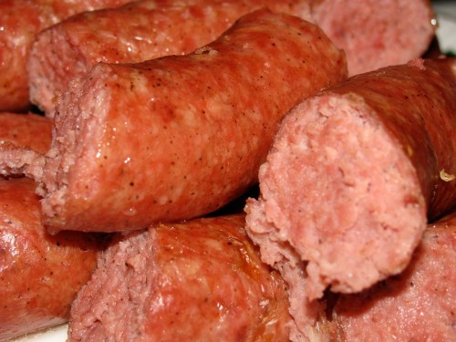 Close-up of sliced sausages, showcasing a pink, meaty interior with a shiny, brown exterior.