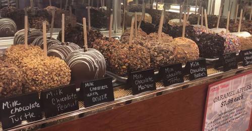 A display of large chocolate-covered treats, including various toppings, with price tags in a candy shop.