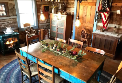 Cozy rustic dining room with a wooden table, chairs, and festive decor, featuring warm lighting and vintage furnishings.