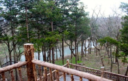 A wooden railing overlooks a serene landscape of trees and a winding river in a peaceful, natural setting.