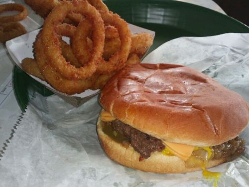 A cheeseburger with melted cheese and a side of crispy onion rings on a green plate.