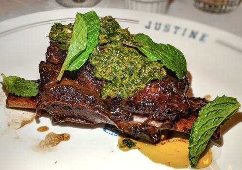 A plate of tender meat with a green herb sauce and fresh mint leaves, served at a restaurant.