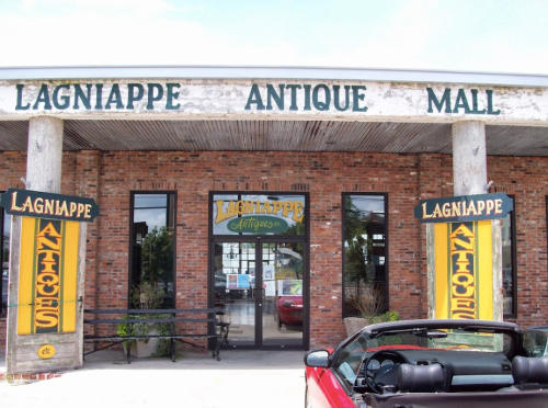 Exterior of Lagniappe Antique Mall featuring brick walls, large signs, and a red convertible parked in front.