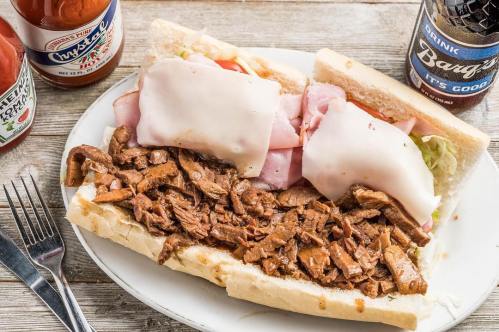 A hearty sandwich filled with sliced meats, cheese, and lettuce, served with condiments and a soda on the side.