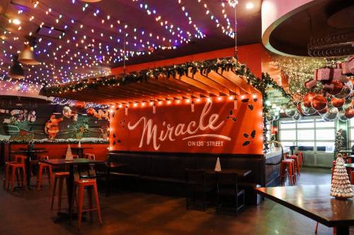 A festive bar interior decorated with colorful lights and holiday ornaments, featuring a sign that reads "Miracle on 135th Street."