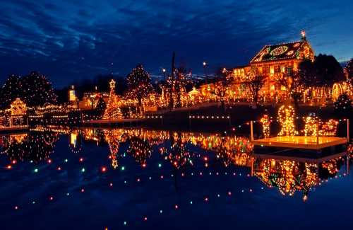 A beautifully decorated house with colorful lights reflecting on a calm lake at dusk.