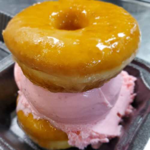 A stacked dessert featuring two glazed donuts with a scoop of pink ice cream in between.
