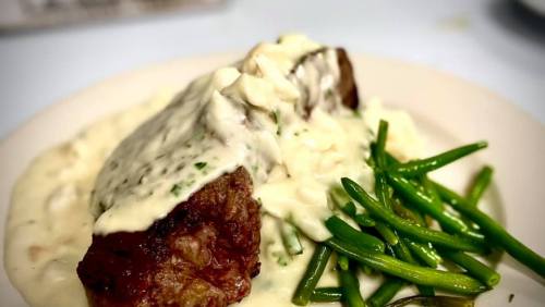 A plate of steak topped with creamy sauce, served with green beans on the side.
