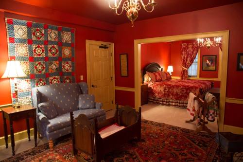 Cozy bedroom with red walls, a quilted wall hanging, a blue armchair, and a wooden crib in a warm, inviting atmosphere.