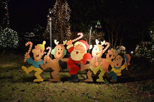 A festive scene featuring Santa and five cheerful characters holding candy canes, surrounded by twinkling holiday lights.