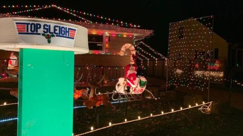 A festive display featuring colorful lights, a Santa on a sleigh, and a sign reading "Top Sleigh" in a nighttime setting.