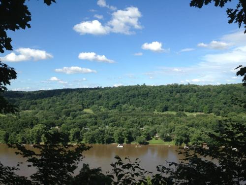 A scenic view of a river surrounded by lush green hills and a blue sky with fluffy clouds.