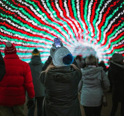 A crowd of people walking through a colorful light tunnel with red and green lights, some taking photos.