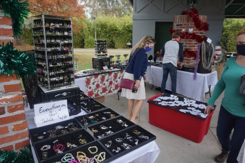 A jewelry market scene with displays of earrings, necklaces, and bracelets. Shoppers browse while wearing masks.