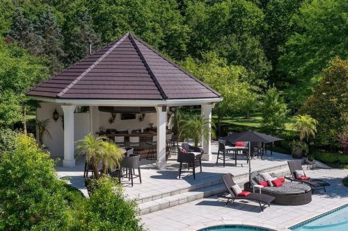 A stylish outdoor gazebo with seating, surrounded by greenery and a pool, creating a relaxing backyard retreat.