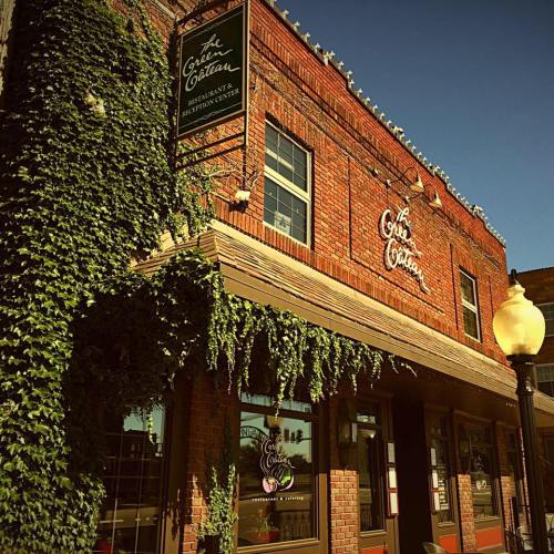 A brick building with ivy, featuring a sign for a restaurant and a lamp post in front under a clear blue sky.