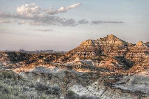 A scenic view of layered rock formations and hills under a soft sky with scattered clouds.