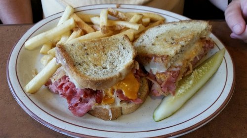 A plate with a sandwich filled with ham and cheese, served with fries and a pickle on the side.