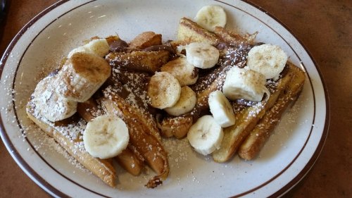 A plate of French toast topped with banana slices, Nutella, and powdered sugar, garnished with cinnamon.