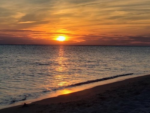 A serene beach at sunset, with vibrant orange and yellow hues reflecting on the calm water.