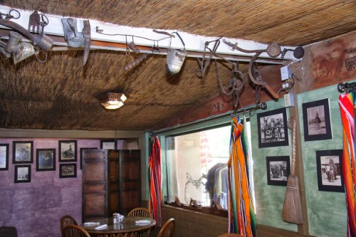Interior of a rustic room with a thatched ceiling, vintage tools hanging, and framed historical photos on the walls.