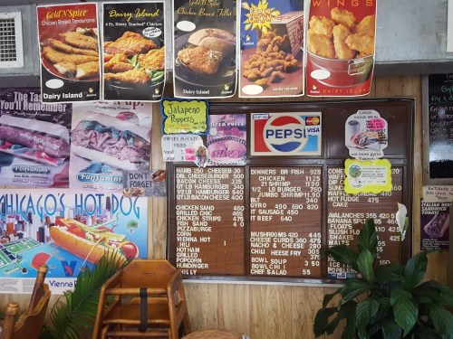 Menu board featuring various food items, surrounded by vintage food posters in a casual dining setting.