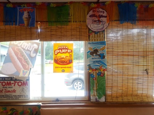 Colorful decorations and posters adorn a window, showcasing food items like hot dogs and pizza puffs in a casual setting.