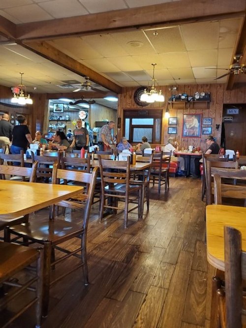 A busy restaurant interior with wooden tables, chairs, and patrons enjoying their meals. Warm, inviting atmosphere.