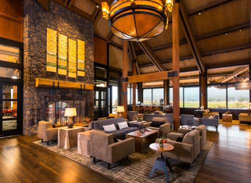 Cozy lodge interior with high wooden ceilings, stone fireplace, and comfortable seating, featuring large windows and warm lighting.
