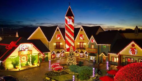 A festive village decorated with colorful Christmas lights and a tall candy-striped tower at dusk.