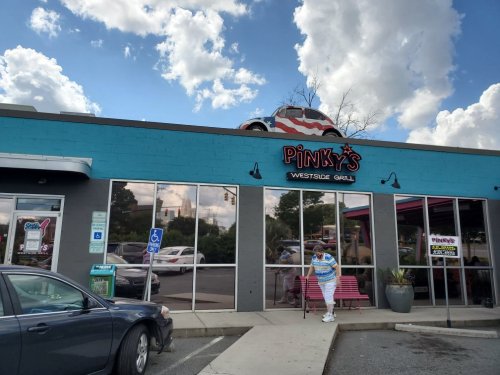 Exterior of Pinky's Westside Grill, featuring a colorful building and a vintage car on the roof under a cloudy sky.