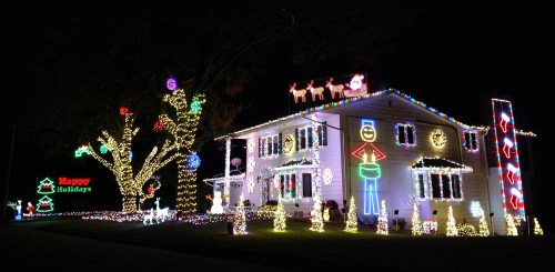 A house decorated with colorful holiday lights, featuring festive figures and a "Happy Holidays" sign.