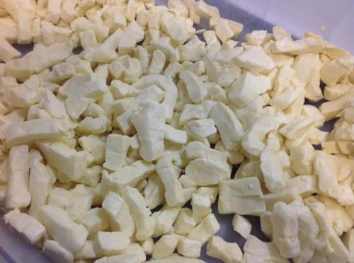 A close-up of small, irregularly shaped pieces of fresh cheese curds in a container.