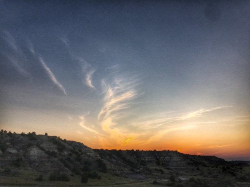 A serene sunset over rolling hills, with wispy clouds and a warm orange glow in the sky.