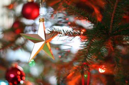 A close-up of a Christmas tree with colorful ornaments and a star decoration, illuminated by warm lights.
