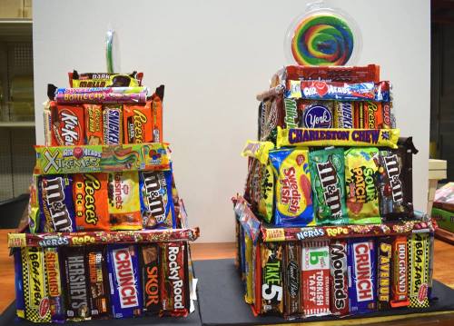 Two colorful candy towers made of various candy bars and a large lollipop on top, displayed on a table.